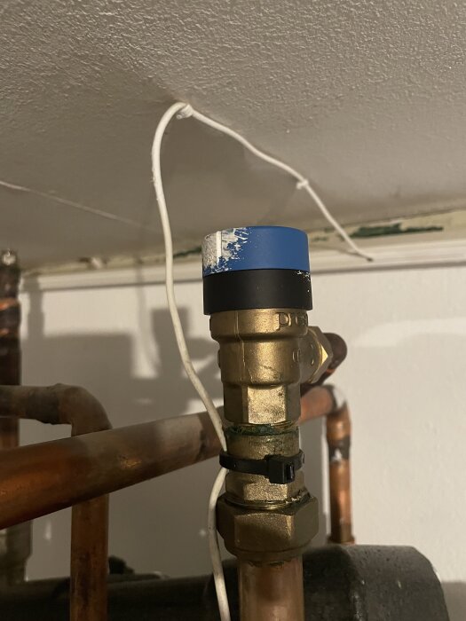 Ventil med blå och svart täckkåpa på ett kopparrör, med pyserandeljud problem ovanifrån och från sidan.
