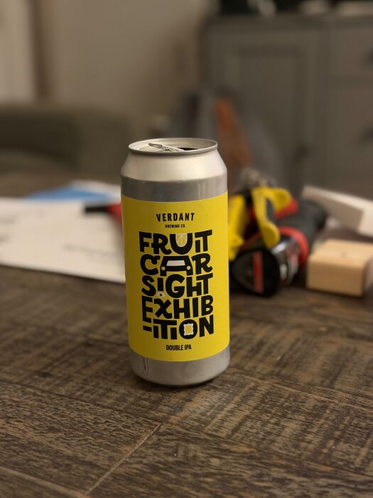 En burk med Double IPA från Verdant Brewing Co. står på ett träbord, omgiven av verktyg och papper i bakgrunden.