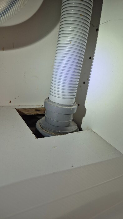 Vit korrugerad slang under diskbänk, ansluten till avloppsrör genom en öppning i skåpbotten, i ett IKEA-kök.