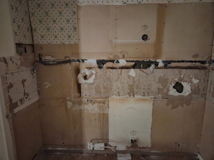 Avrivet kök med skadade väggar och synliga kablar. Kakel har tagits bort och bakomliggande ytor är ojämna och slitna.