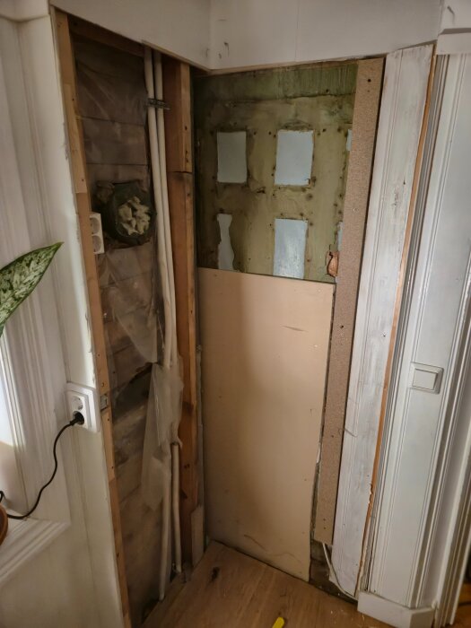 Vägg med avskalad panel, synliga rör och trasig isolering efter rivning av kök.