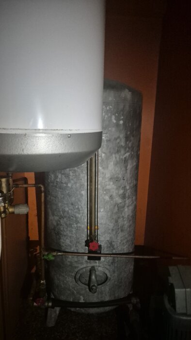 Vattenpump med rör och ventiler i ett grått rum, diskussion om brunnar och pumpsystem i en fastighet.