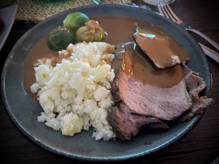 Tallrik med porterstek, täckt med sås, serverad med pressad potatis och brysselkål.