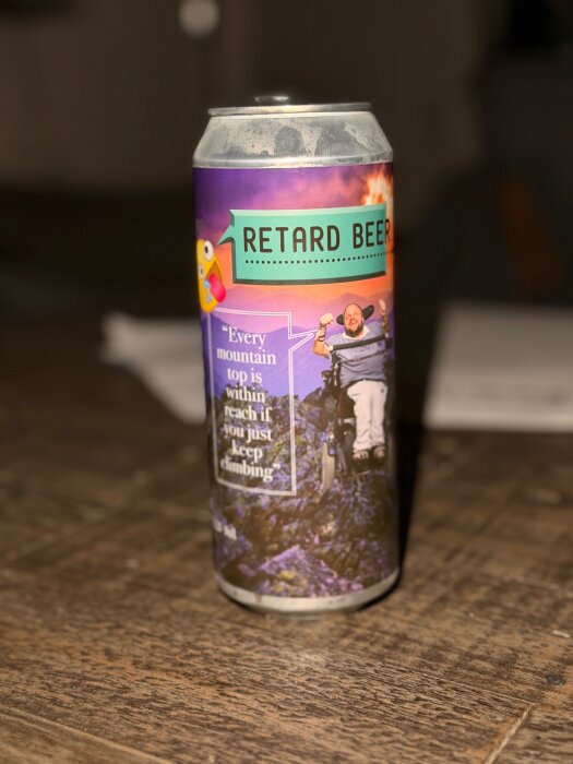 En burk med etiketten "Retard Beer" och en bild av en man på en bergstopp. Text inkluderar "Every mountain top is within reach if you just keep climbing.