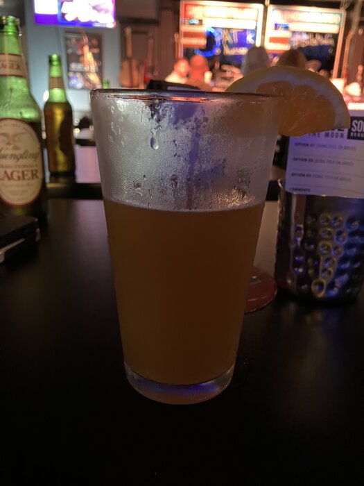 Ölglas med skiva av apelsin på kanten på en bar. Flaskor och oskarp bakgrund med skarpa ljus och instrument.