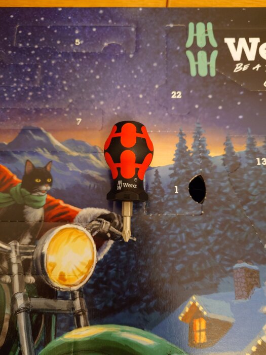Skruvmejsel från Wera framför en adventskalender med ett vinterlandskap och en katt i tomtedräkt som kör motorcykel.