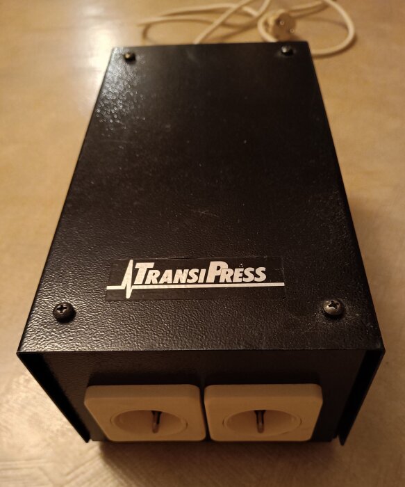 Svart transformatorlåda från TransiPress med två uttag, använd av audiofiler för att förbättra ljudkvaliteten, stående på ett bord.