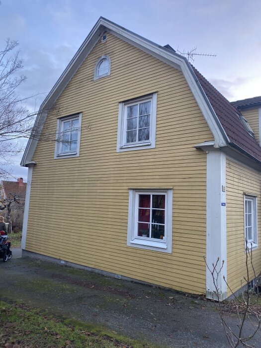 Gult trähus med vita fönster och brunt tak, beläget i Nyköping. Huset har asymmetriska fönster som ger ett kompakt intryck.
