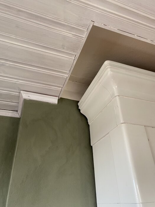 Kakelugn med vit detalj i taket, gröna väggar och spår av takhöjdsjustering.