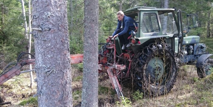 Person sitter på en traktor med rymlig hytt i skogen, nära ett träd.