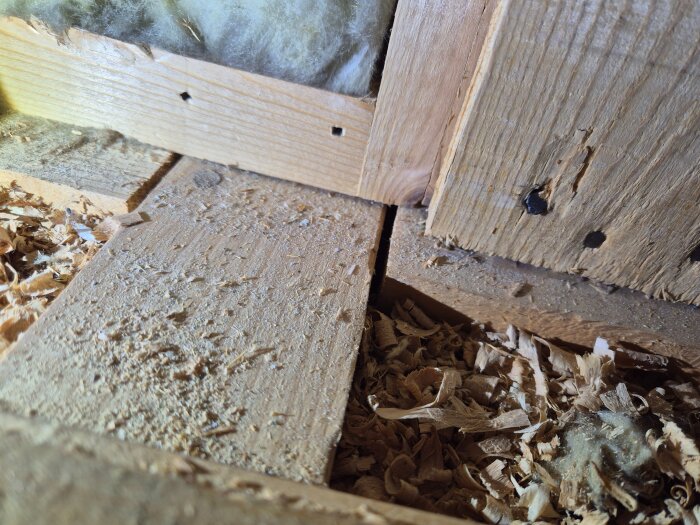 Close-up of wooden attic construction with exposed insulation and shavings, showing a gap between boards; context of planning an attic expansion.