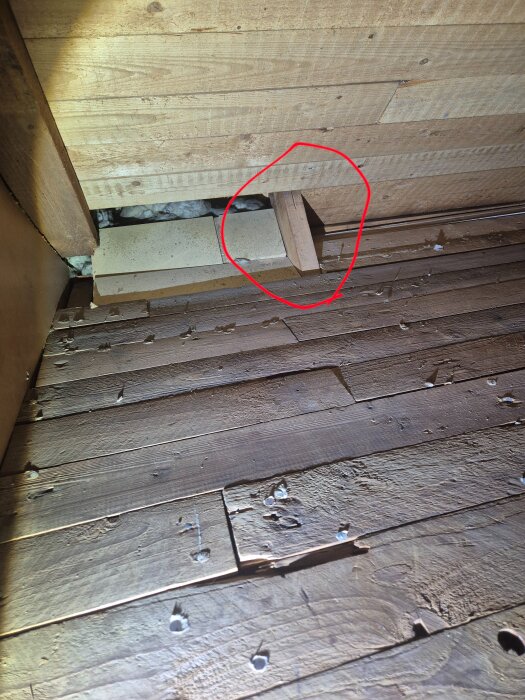 Insida av en vind med träväggar och golv, där en sektion av väggen har öppnats. En röd cirkel markerar ett misstänkt bärande element.