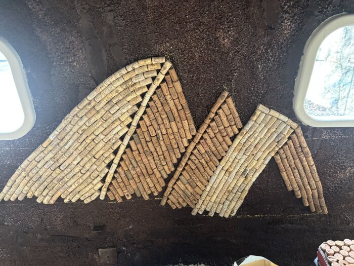 Korklimning på vägg avbildar isberg i himmel och havsmotiv med liggande och stående korkar. Två fönster syns i övre hörnen.