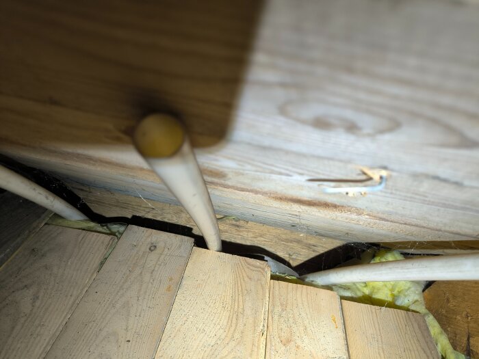 Fuktiga träplankor och rör i en vägg med isolering av glasfiber och kutterspån under; fuktproblem tidigare åtgärdade.