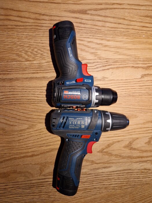 Två skruvdragare av märket Bosch, modell 12V-15 och 12V-32, placerade sida vid sida på ett träbord.