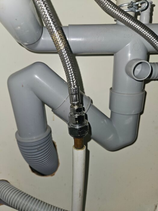 VVS-installation under diskbänk med rör och olika kopplingar, inklusive en flexibel slang och plaströr.