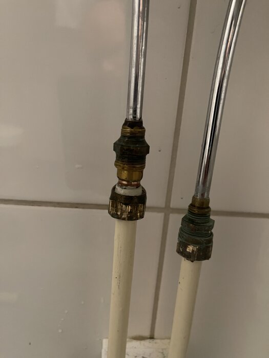 Två vita rör med metallgängor kopplade till två silverfärgade rör under ett handfat i ett badrum.