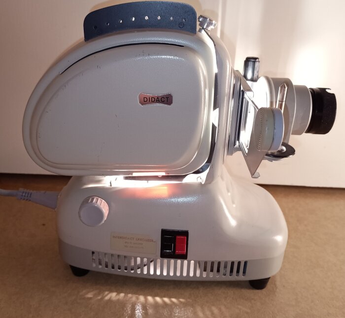 Gammaldags projektor för diaramar och bildband, märkt "Didact", med en retro design och manuell fokusering.