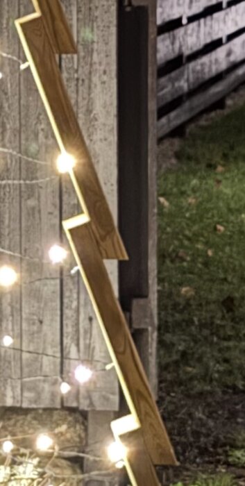 Träregel i zickzackmönster med monterad ljusslinga lutar mot en trävägg.