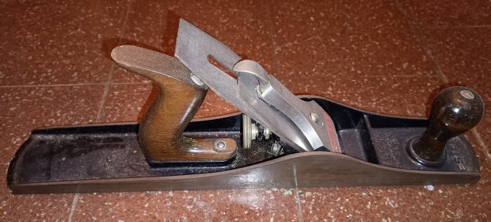 Gammal Esteel hyvel från Eskilstuna med trähandtag och metallblad på brun kakelgolv.
