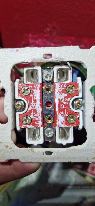 Eluttag med exponerade kablar där jordkabeln inte är inkopplad; omgiven av röd vägg och vit plastram.