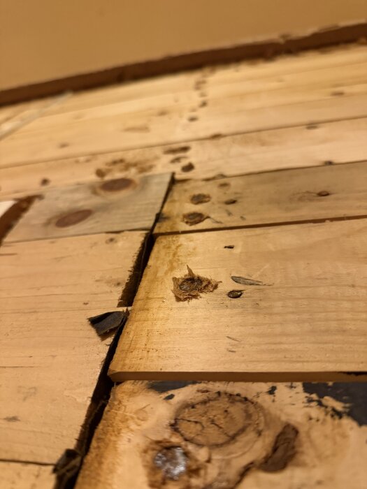 Liggande träplankor med ojämnheter och spikhuvuden på väggen i ett gammalt hus, synliga efter att kök och panel rivits ut.