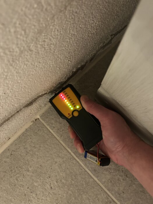 Hand håller en fuktmätare mot en putsad siporex-vägg i ett pannrum, röd lampa lyser vilket indikerar fuktproblem.
