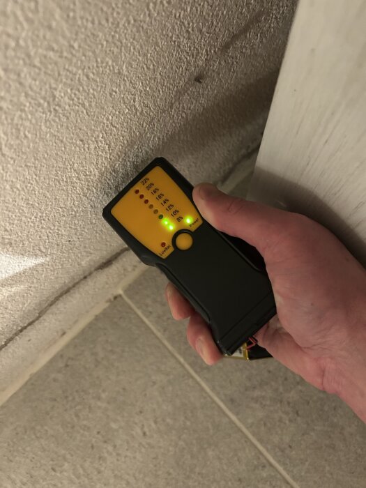 Hand håller en fuktmätare mot en siporexvägg, mätaren visar flera gröna dioder vid lägre fuktnivåer.
