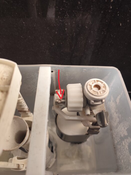 Närbild av insidan av en toalettcisterntank med en pil markerande en läckande del där vatten sprutar ut.