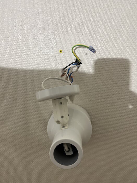 Vägg med en elektrisk anslutning för en sänglampa, kablar sticker ut, potentiellt för borttagning eller omläggning i sovrumsrenovering.