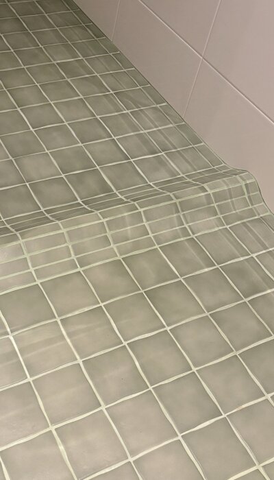 Gröna klinkerplattor i vågmönster på badrumsgolv, detaljerat fokus på fogarna och plattsättning.