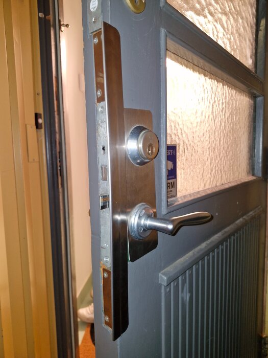 Ytterdörr med ett kromat dörrhandtag och ett cylinderlås, dörrens kant visar låskolven och låsstången, även slutblecket är synligt.