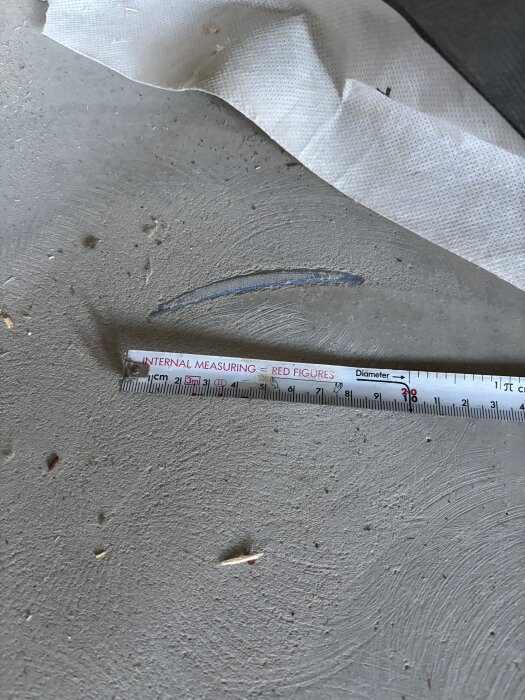 Skadat golvvärmerör synligt i flytspackel, mätsticka visar cirka 29 cm längd vilket demonstrerar problemet med låg täckning och skador på rören.