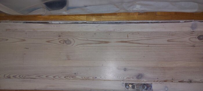 Gammal trätröskel med synliga slitningar och ojämnheter, jämte en nyare parkettgolv som ligger i nivå.