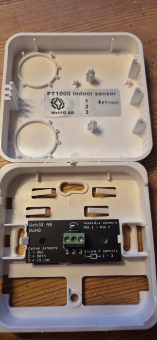 Inuti en PT1000 rumsgivare med öppen hölje, visa tre anslutningsterminaler märkta GND, data, och +5 Vdc.