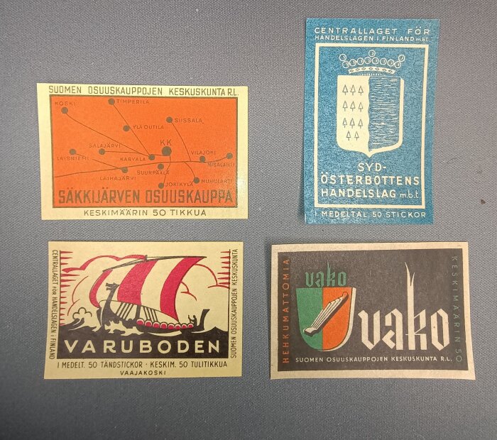 Fyra gamla etiketter från tändsticksaskar med olika mönster och text på finska, inklusive kartmotiv och vikingaskepp.