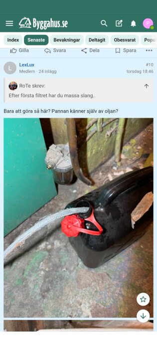 En svart dunk med röd kork kopplad till en slang som leder till ett filter, i ett verkstads- eller pannrum.