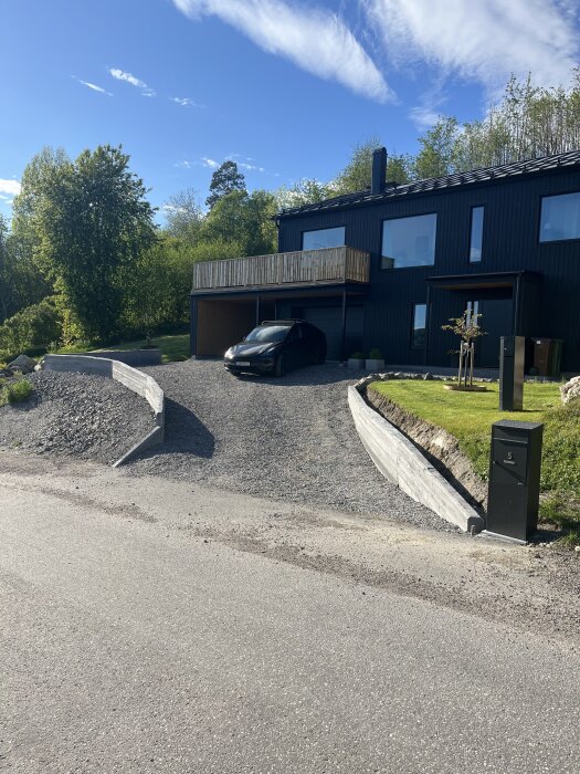 Uppfart med nygjuten stödmur, svart bil parkerad framför ett modernt hus, omgiven av grönska och blå himmel.