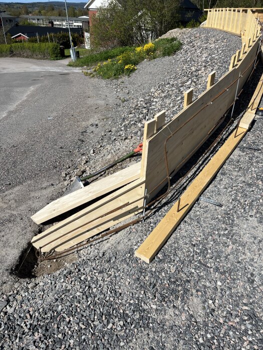 Form för murbyggnation med trästöd och armeringsjärn på en grusväg.