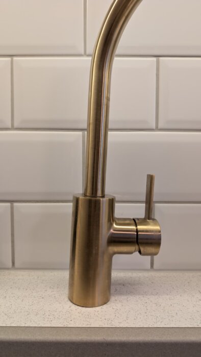 Kökskran av metall lutande på en deformerad diskbänk, synlig med vit kakelbakgrund.