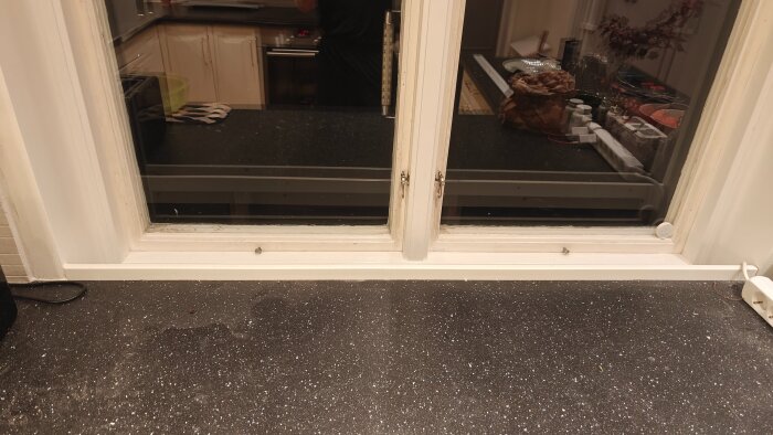 Köksbänk intill fönster med liten vit sarg, inga synliga bakstycken på skåpen, och mörk bänkskiva. Utsikt mot köket.