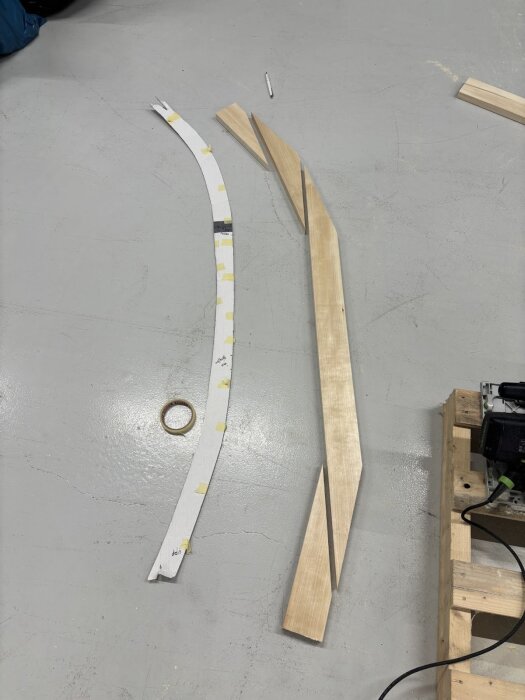 Mall av wellpapp och trästycken i olika vinklar ligger på golvet; förberedelse för dörrkarmens kurvatur.