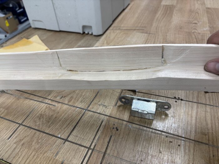 Träbit med urfräst spår för låsbleck på träbord, brevid ligger låsanordning.