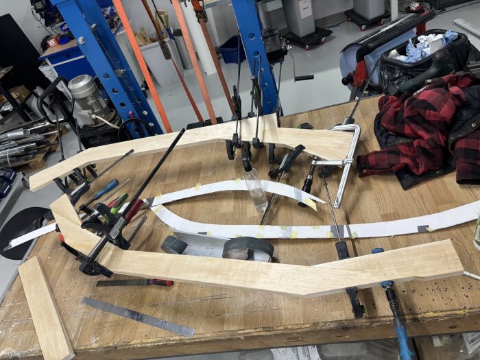 Trädelar under tillverkning med hjälp av mallar och tvingar, verktyg och material runt omkring på arbetsbänken i en verkstadsmiljö.