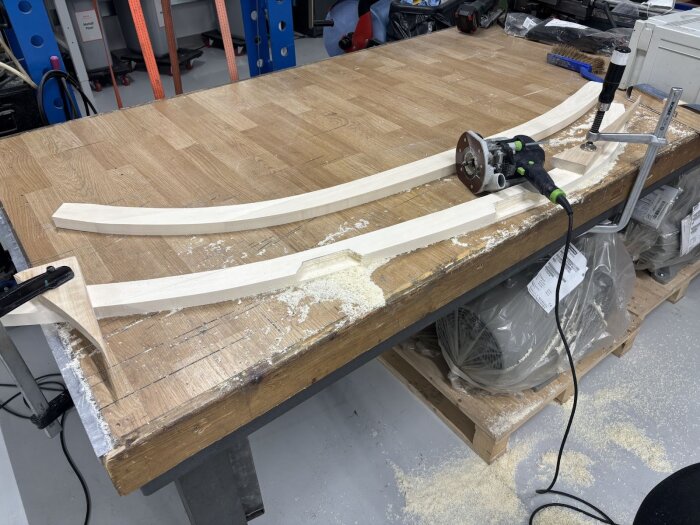 Trädelar och en fräsmaskin på ett arbetsbord, sidostycken till dörrkarmar bearbetas för anpassning till vagnens kurvatur.