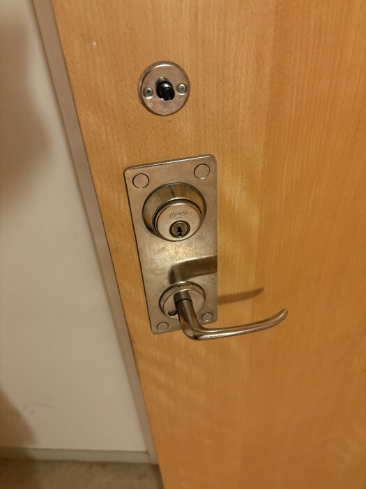 Ytterdörr med ett metallhandtag och ett slitet lås som behöver bytas ut, enligt inlägget om problem med låset.