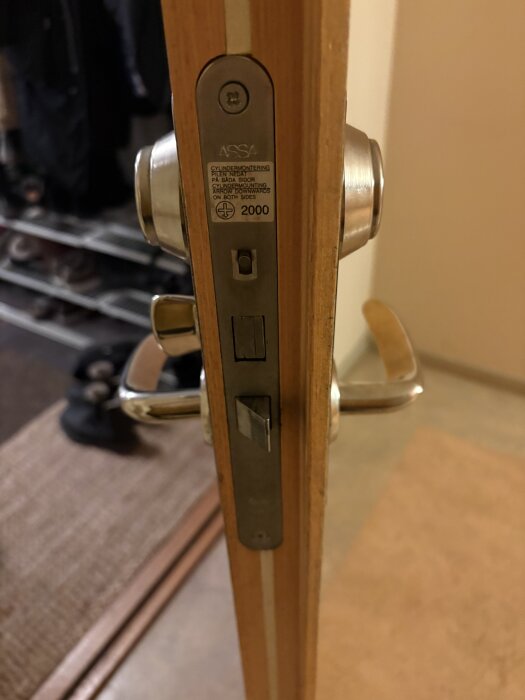 Närbild på en öppnad dörr med ett slitet ASSA-lås och dörrhandtag. Låsdetaljerna syns tydligt, handtaget verkar slappt.