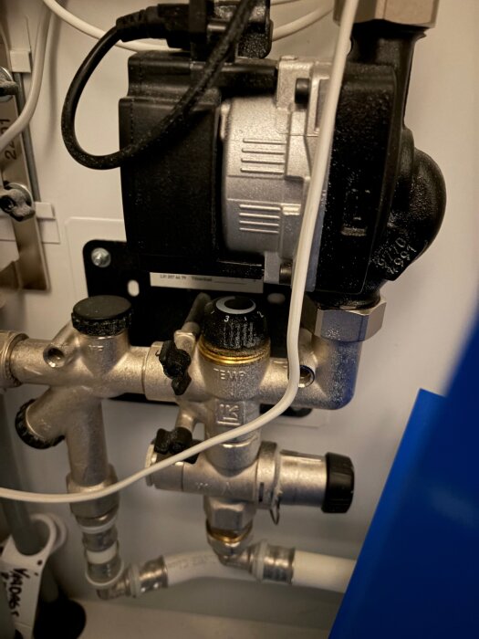 Golvvärmesystem med rör, ventiler och en cirkulationspump i ett skåp, del av golvvärmeinspektion för att lösa värmeproblem i hemmet.