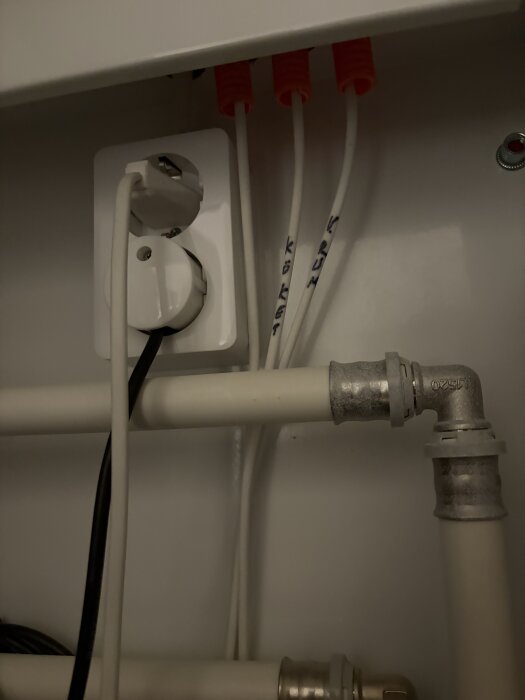 Eluttag med sladdar och rör i ett skåp. Sladdarna är märkta med "KÖKET" och "K-RUM".