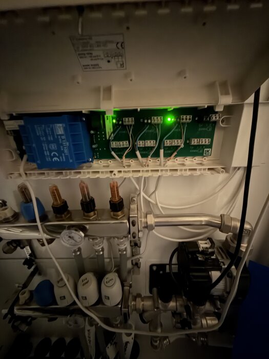 Elcentral med grönt ljus, kablar och rör synliga; relaterat till värmeproblem i badrum och vardagsrum.